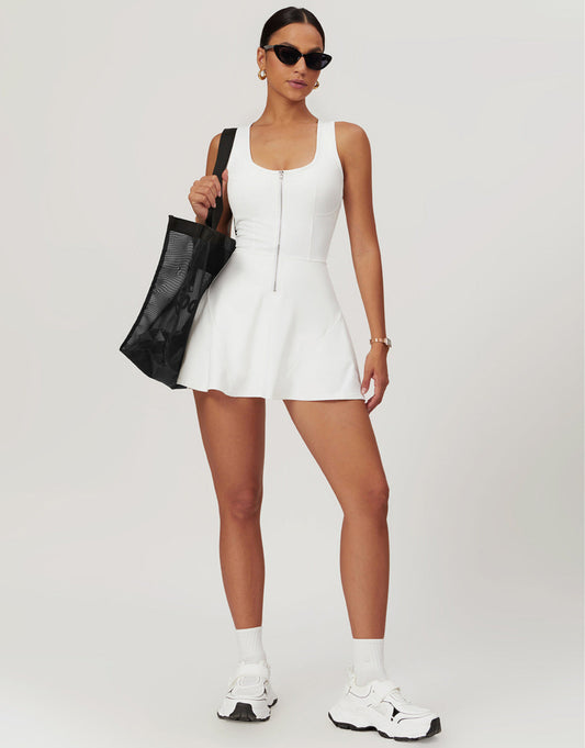 Woman in a white dress holding a black bag on a plain background